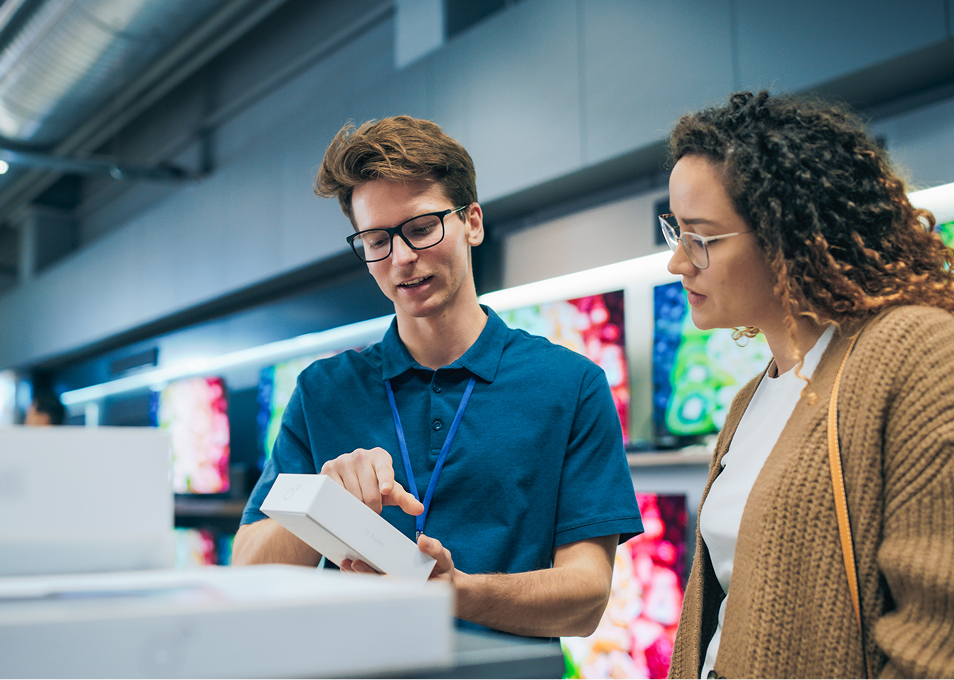Clerk shows boxed item to customer in electronics store.